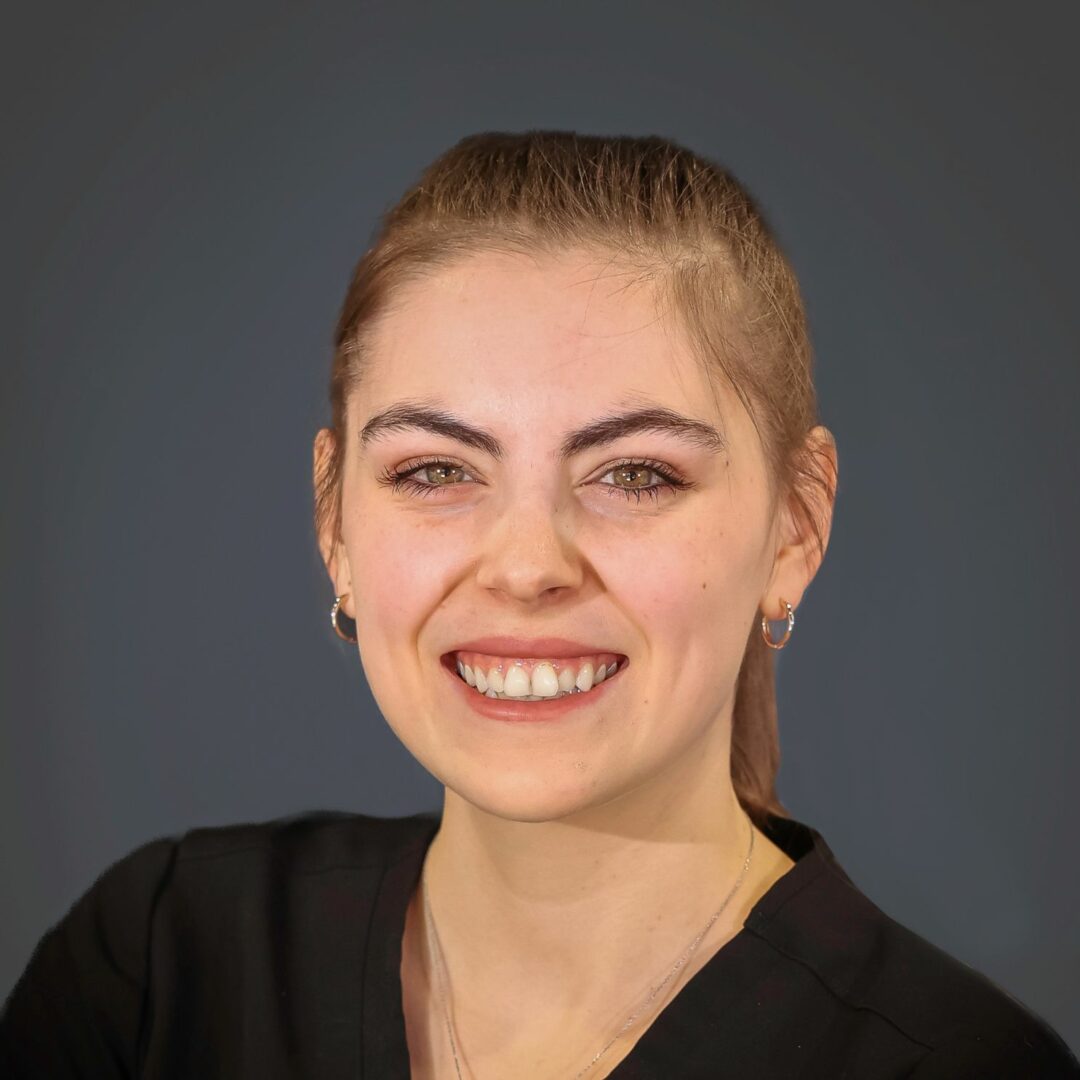 portrait of Maura of Natural Endocrinology Specialists in black scrubs smiling on a dark grey background